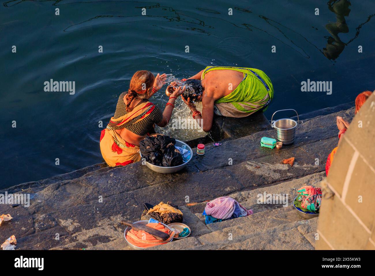 Zwei indische Frauen in farbenfrohen Saris stehen im Fluss narmada auf den maheshwar-Ghats, die ihre Haare waschen Stockfoto