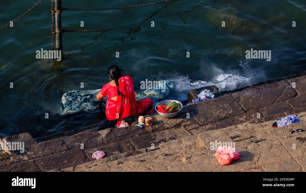 Eine indianerin in einem knallroten Sari wäscht ihre Kleider im heiligen Wasser des Flusses narmada von den ghats von maheshwar Stockfoto