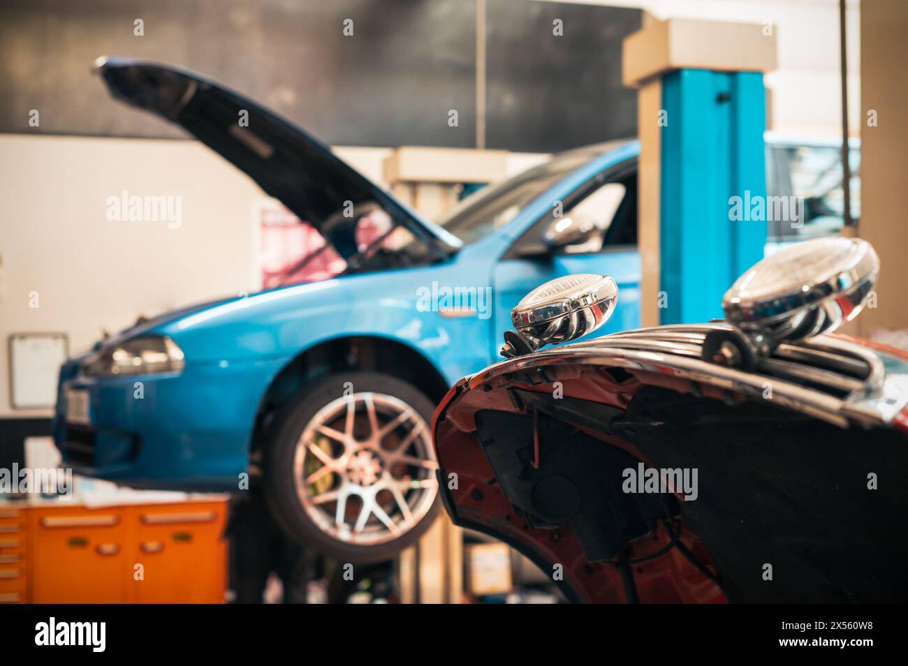 Angehobenes Fahrzeug mit geöffneter Motorhaube und Reflexion auf dem Fensterglas während der Reparaturwerkstatt einer Garage, die mit verschiedenen Instrumenten für Service und ausgestattet ist Stockfoto