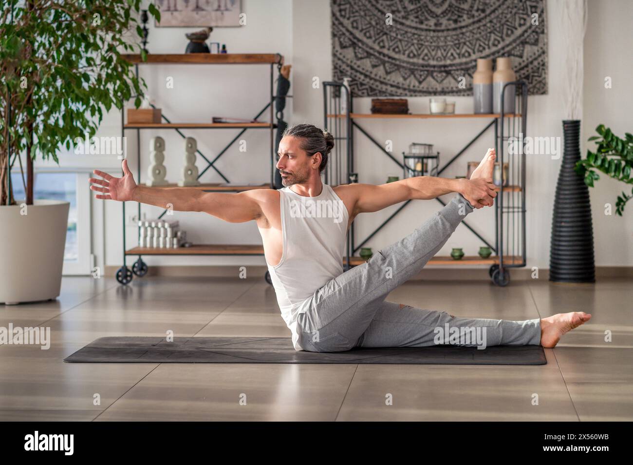 Seitenansicht eines starken männlichen Erwachsenen in Sportbekleidung, der wegschaut, während er in der sich drehenden, sitzenden Hand auf der Matte sitzt und in der Halle Sport macht Stockfoto