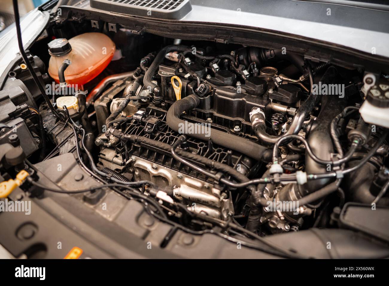 Von oben sichtbarer staubiger Pkw-Motor unter geöffneter Motorhaube mit verschiedenen montierten Ersatzteilen, während elektrische Kabel mit der Batterie und in Service s verbunden sind Stockfoto