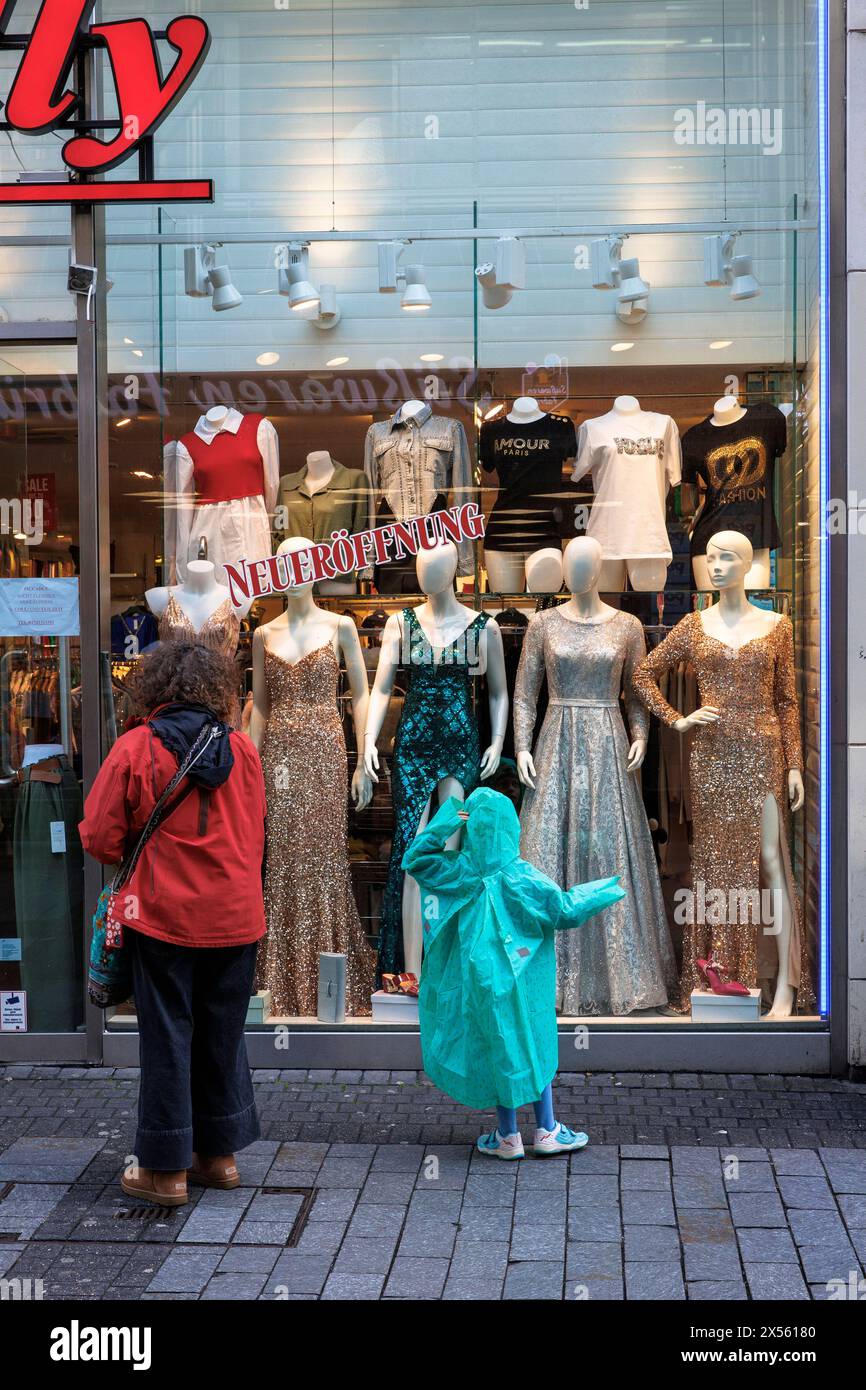 Ein Kind im Regenmantel und eine Frau schauen sich Kleidung in einem Schaufenster in der Einkaufsstraße hohe Straße, Köln an. ein Kind in einem Regenmantel Stockfoto