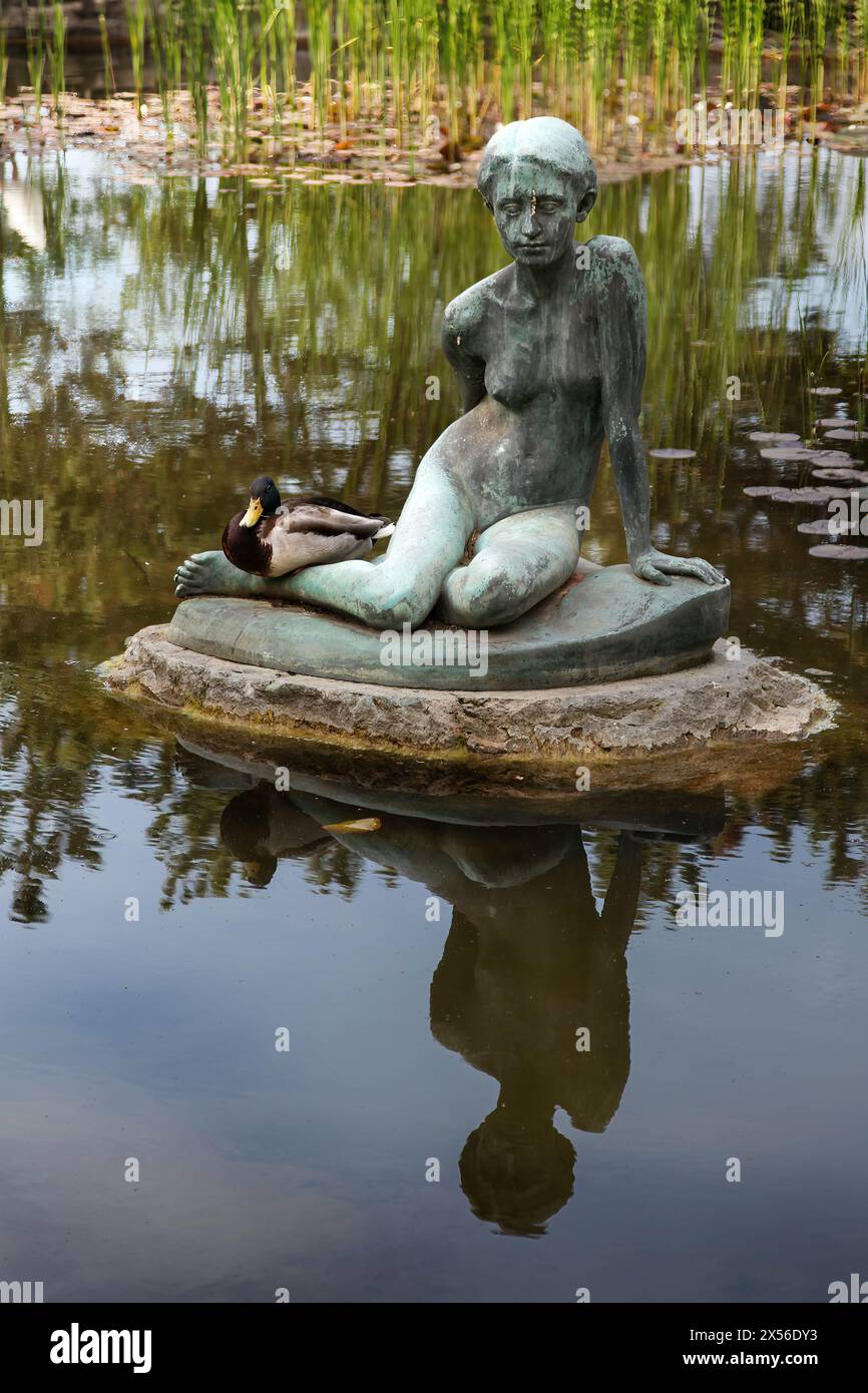 Statue eines sitzenden Mädchens, mit einer echten Ente an der Seite, im Wasser eines Teichs im Japanischen Garten, Margareteninsel Stockfoto