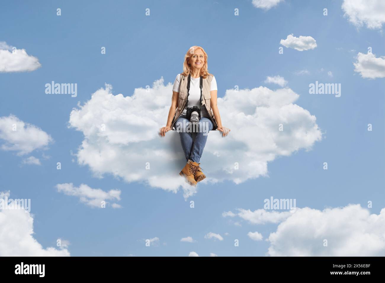 Weibliche Fotoreporterin sitzt auf einer Wolke und lächelt Stockfoto