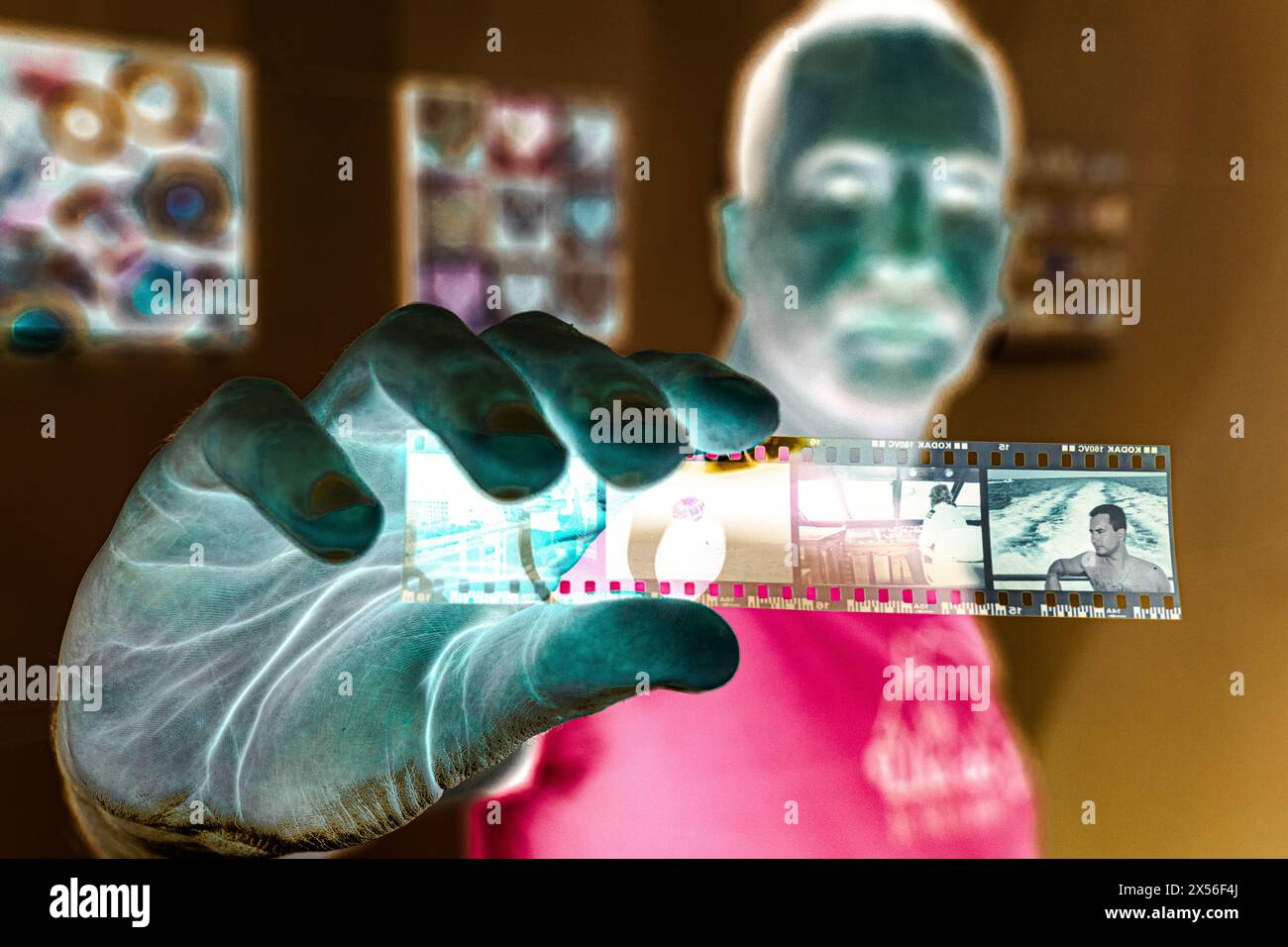50-jähriger weißer Mann, der 35 mm Negativfilm mit seinem 30 Jahre jüngeren Bild zeigt, die Farben sind invertiert. Stockfoto