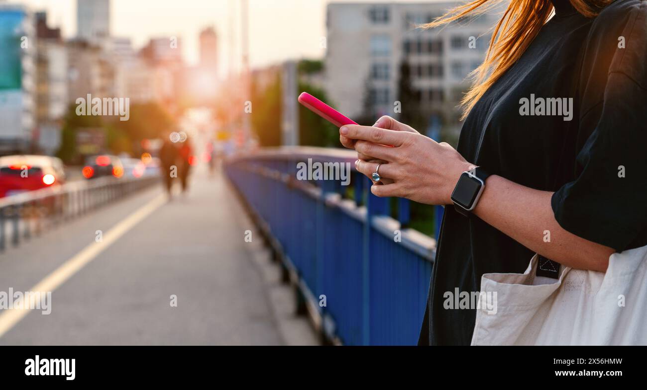 Weibliche Person steht auf der Stadtbrücke und sendet online Nachrichten mit ihrem Smartphone. 5G-Technologie in der Stadt. Stockfoto