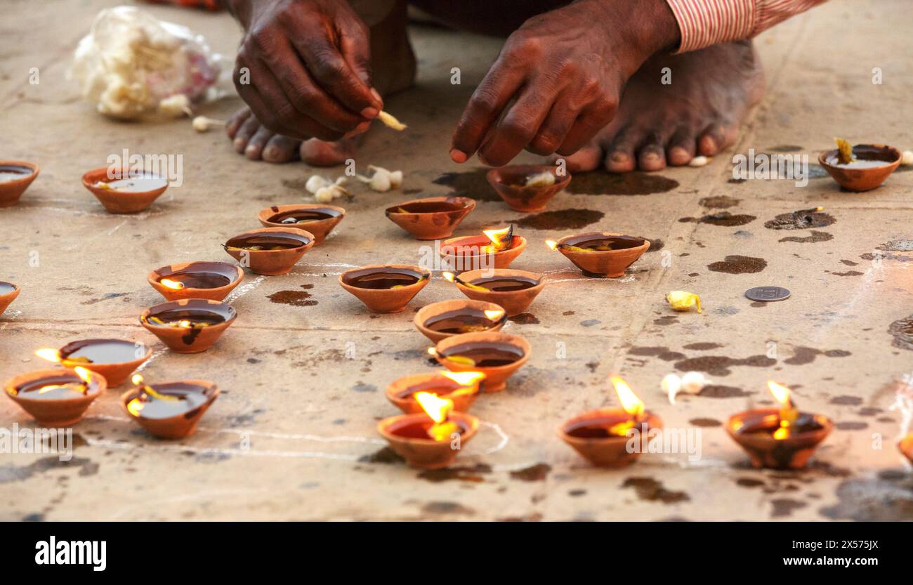 Füße und Hände eines Pilgers, der kleine Öllampen in Tonschalen neben dem Ganges in Varanasi, Indien, anzündet. Stockfoto