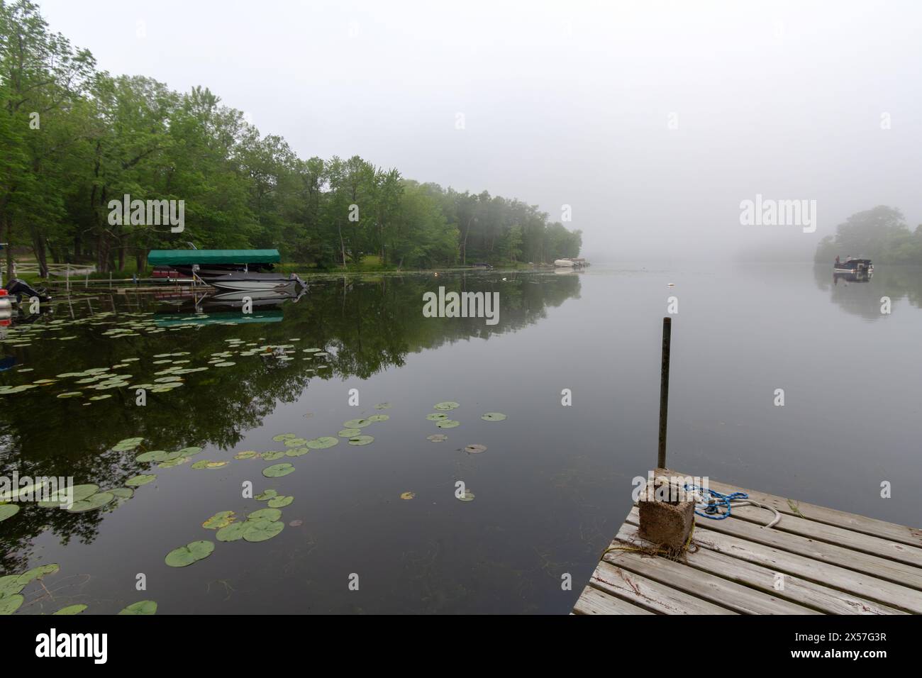 Blick von der Ecke eines Piers auf einen ruhigen Wisconsin See an einem nebeligen Morgen. Fischerboot in der Ferne. Stockfoto