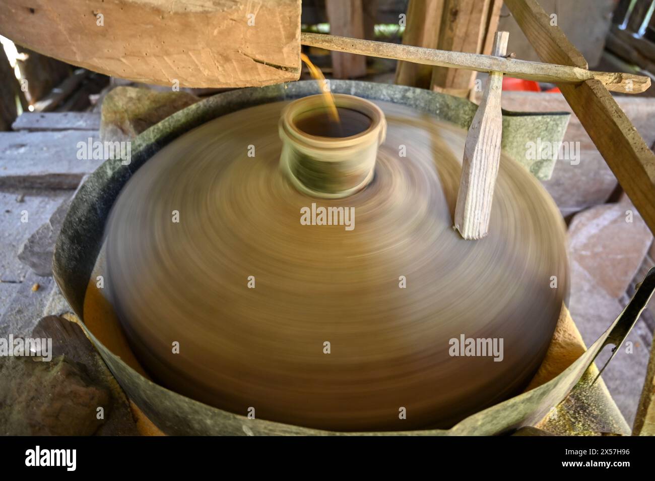 Ein Mühlstein dreht sich. Ein Stein mahlt Korn in einer Mühle. Herstellung von Maismehl. Maiskörner fallen in die Mühle. Traditionelle Wassermühle am Fluss Stockfoto