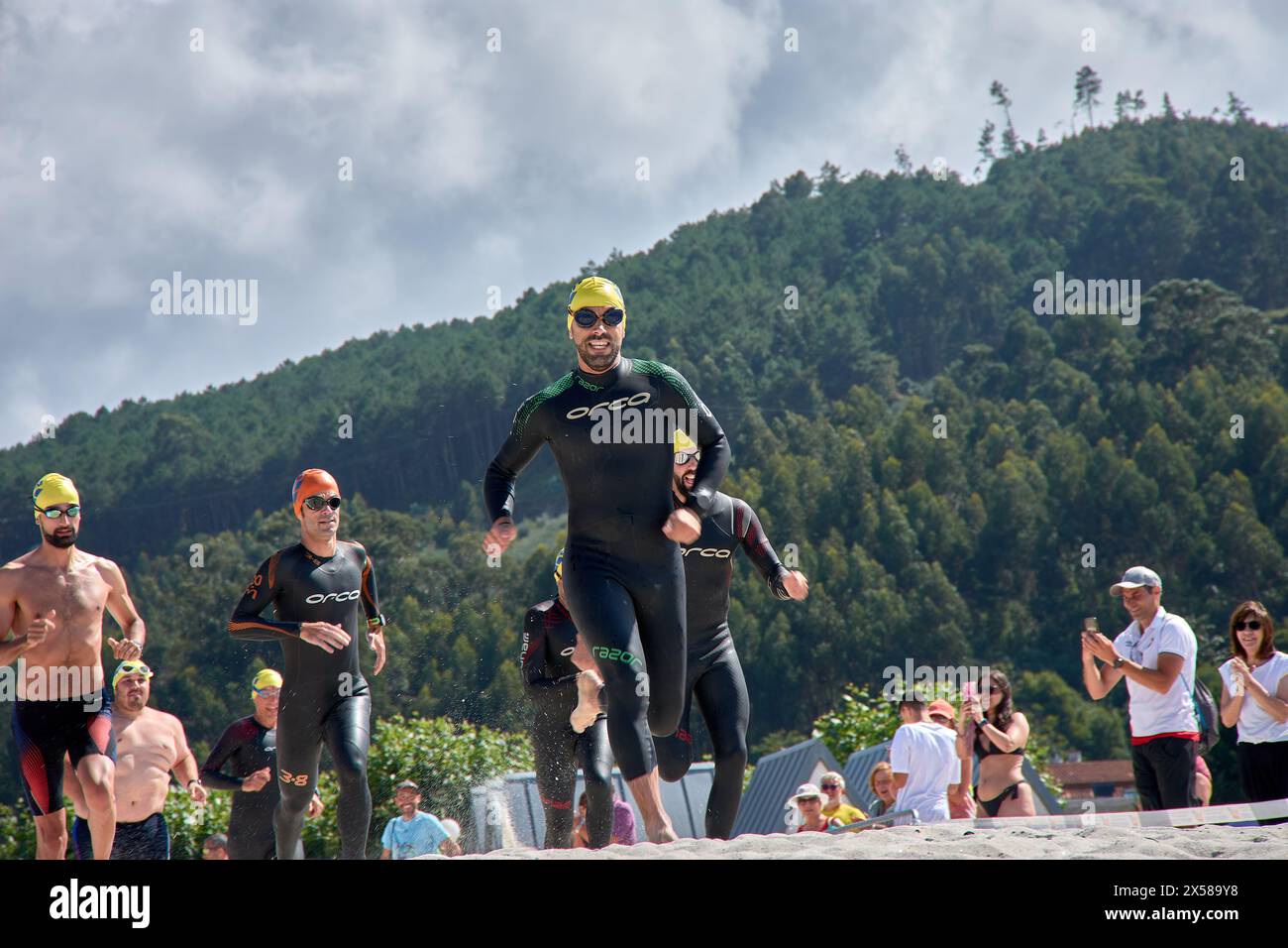 Sabaris, Baiona, Pontevedra, Spanien; 15. Juli, 2023: Triathlon-Teilnehmer laufen durch den Strand von Ladeira in Richtung Wasser, um mit dem Schwimmen zu beginnen Stockfoto