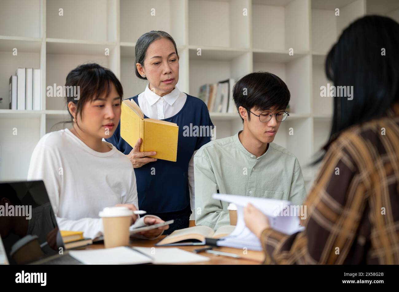 Eine strenge asiatische Professorin oder Lehrerin unterrichtet ihre Schüler im Klassenzimmer. Eine Gruppe von Studenten einer Universität, die mit einem Reifen f Stockfoto