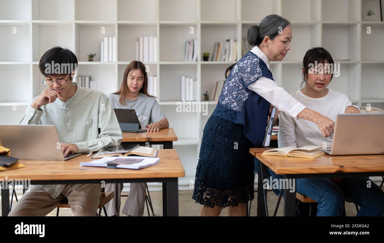 Eine erfahrene und professionelle, reife asiatische Lehrerin oder Professorin, die Schüler im Klassenzimmer unterrichtet und ihrer Schülerin bei einer schwierigen Mathematik hilft Stockfoto