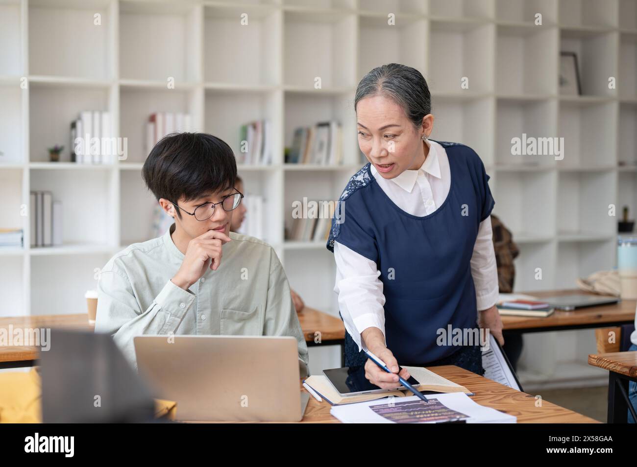 Eine reife asiatische Lehrerin, die ihrer Schülerin in der Klasse hilft und schwierige mathematische Probleme erklärt. Bildungskonzept Stockfoto