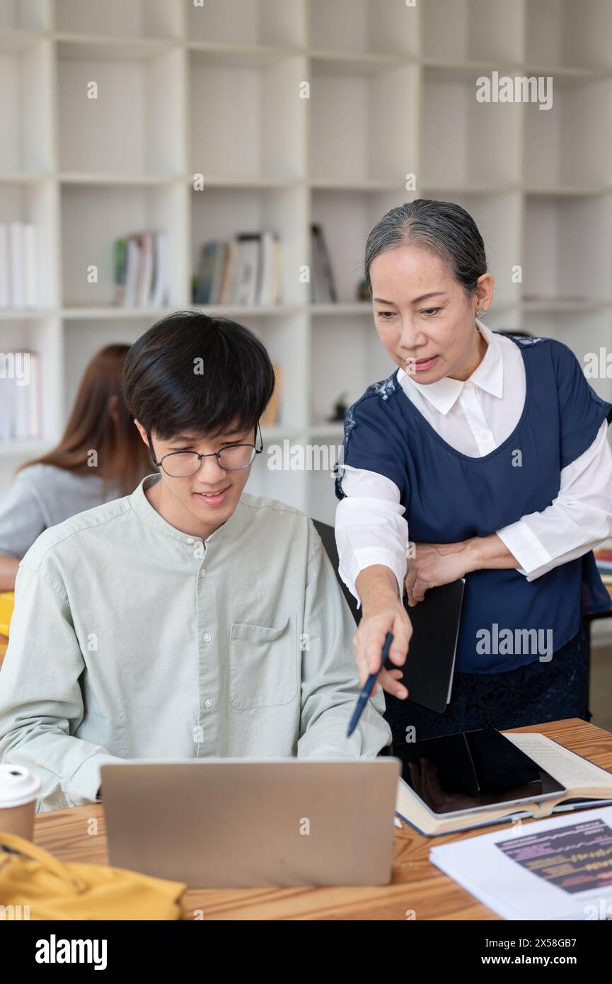 Eine reife asiatische Lehrerin, die ihrer Schülerin in der Klasse hilft und schwierige mathematische Probleme erklärt. Bildungskonzept Stockfoto