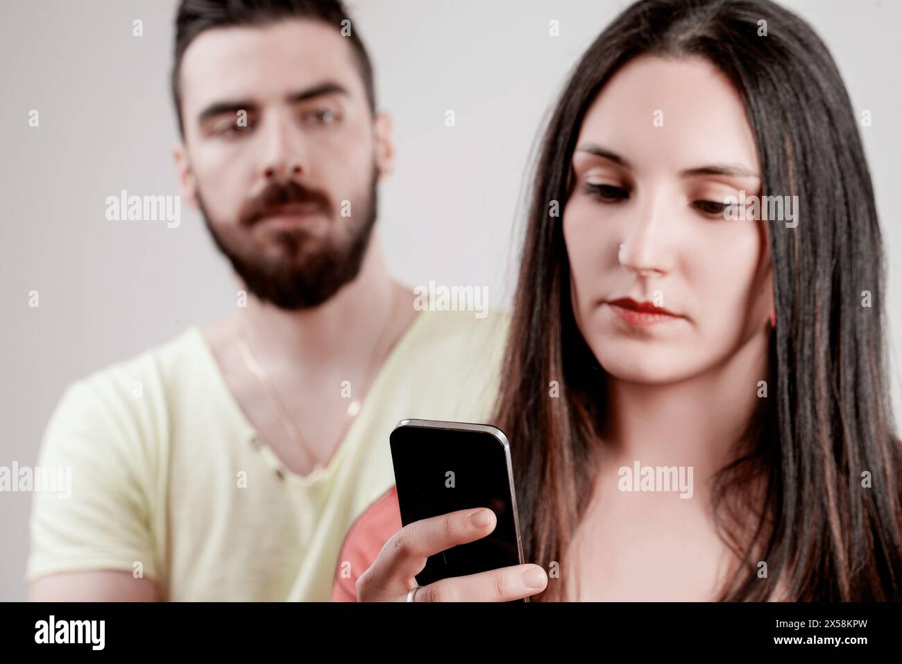 Die eifersüchtige Wachsamkeit des Mannes durch sein Smartphone steht im Widerspruch zum unruhigen Blick seines Partners und deutet auf tiefere Probleme in seiner Beziehung hin Stockfoto