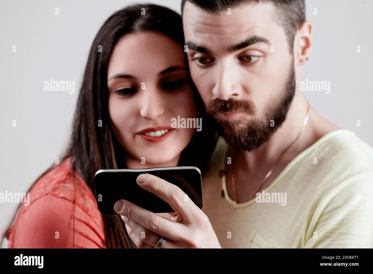 Mann und Frau genießen Inhalte auf einem Smartphone, ihr fröhliches Lachen und sein fokussierter Ausdruck heben einen Moment der gemeinsamen digitalen Interaktion hervor Stockfoto