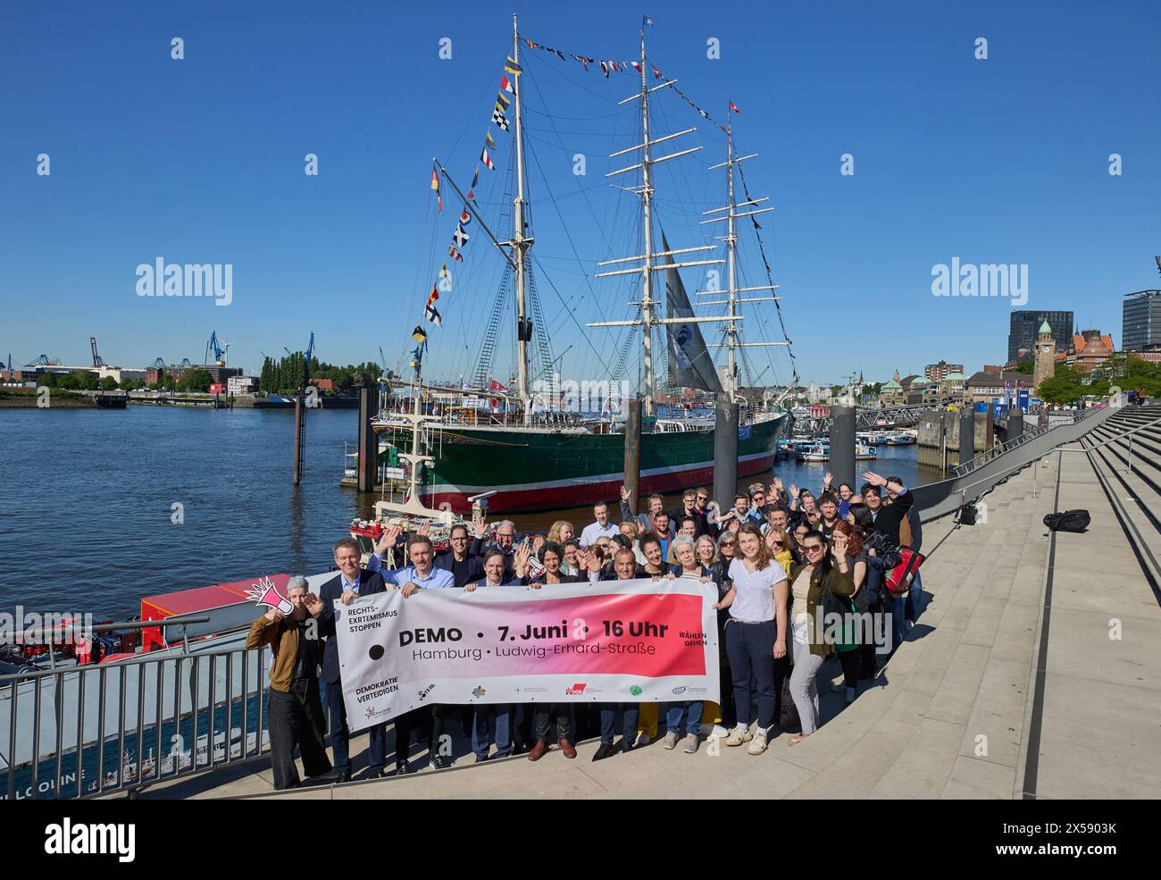 Hamburg, Deutschland. Mai 2024. Teilnehmer einer Fotosession der Hamburger Allianz "Rechtsextremismus stoppen - Demokratie verteidigen - Abstimmung" stehen im Hafen an der Jan-Fedder-Promenade und halten ein Banner mit der Aufschrift "Demo 7. Juni, 16 Uhr Hamburg Ludwig-Erhard-Straße". Im Hintergrund kann man das Museum und das Denkmalschiff Rickmer Rickmers sehen. Quelle: Georg Wendt/dpa/Alamy Live News Stockfoto