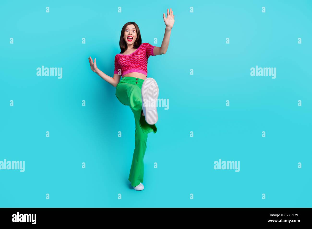 Foto in voller Länge der erstaunten lustigen netten Frau gekleidete Oberteil grüne Hosen zeigen Schuhe, die zurück fallen isoliert auf blauem Hintergrund Stockfoto