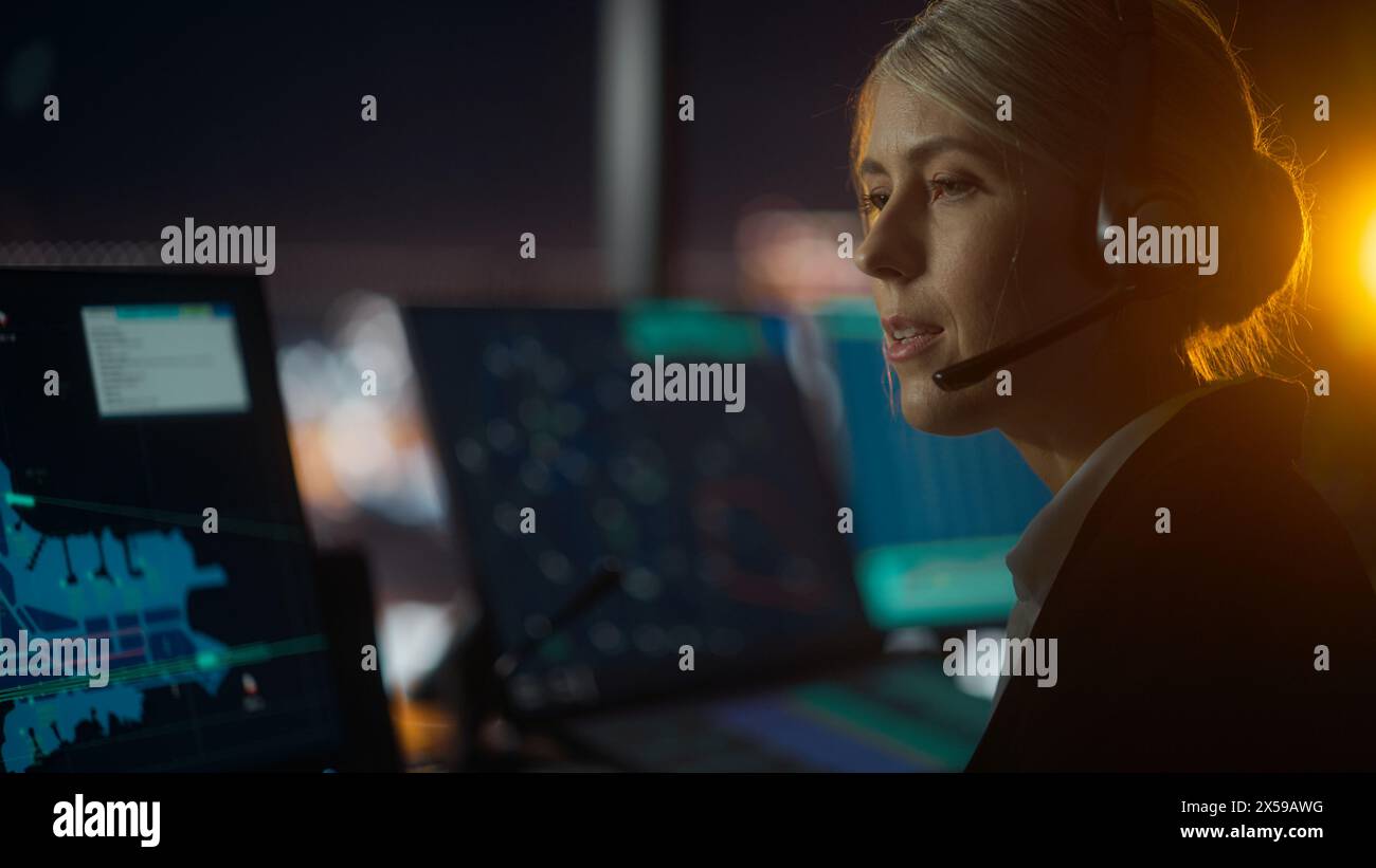 Nahaufnahme weibliches Porträt der Fluglotse mit Headset bei einem Anruf im Flughafenturm bei Nacht sprechen. Der Büroraum ist voll von Computerdisplays mit Navigationsbildschirmen, Flugradardaten. Stockfoto