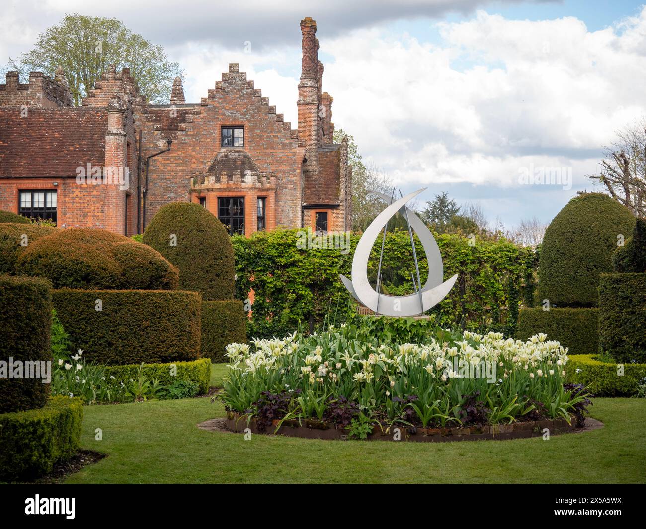 Chenies Manor House aus dem Topiary Garden mit Skulpturen und weißen Tulpen in einem runden Blumenbeet. Stockfoto