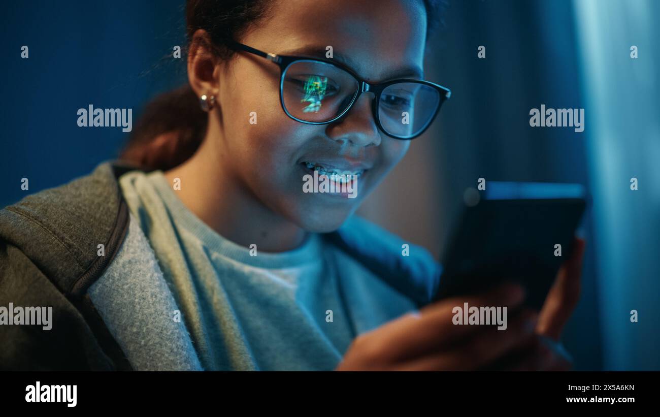 Porträt eines Jugendlichen multiethnischen Schwarzen Mädchens, das ein Arcade-Videospiel auf einer Smartphone-Anwendung spielt. Sie trägt Brillen und Zahnspangen. Stockfoto