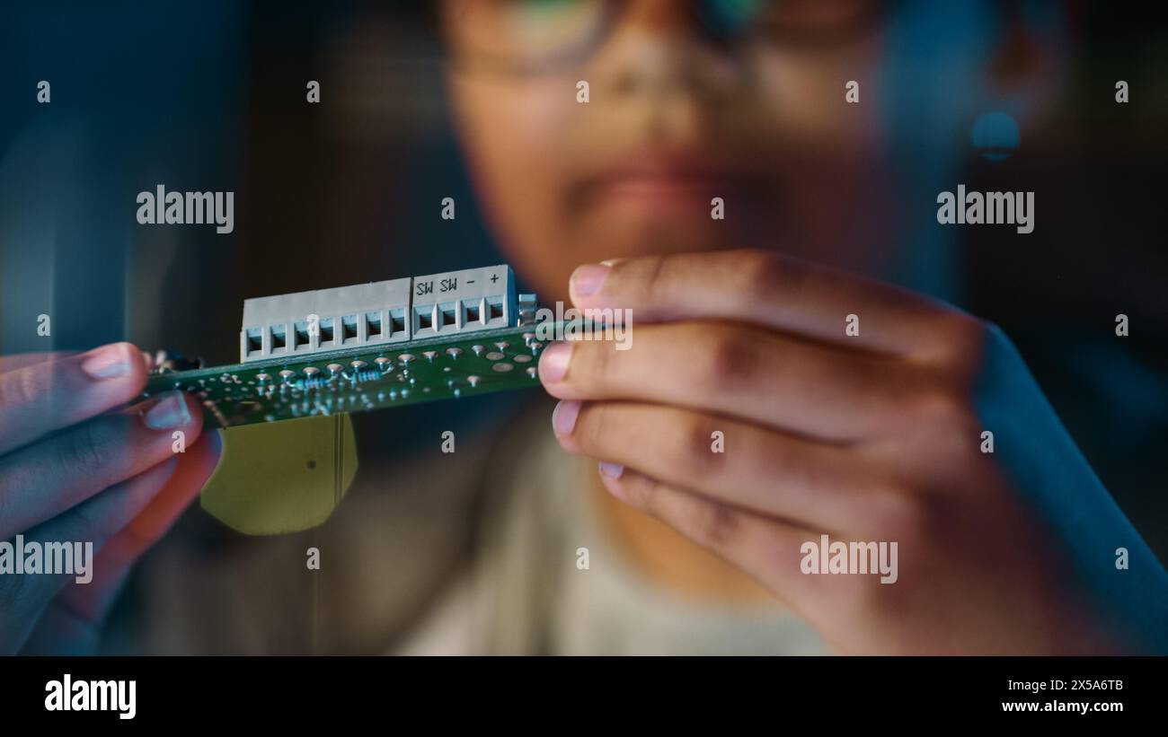 Nahaufnahme Porträt eines süßen jungen, multiethnischen Schwarzen Mädchens im Teenageralter studiert ein kleines Leiterplattenobjekt. Junge Frau trägt Brille und arbeitet an ihrem Schulwissenschaftsprojekt. Stockfoto