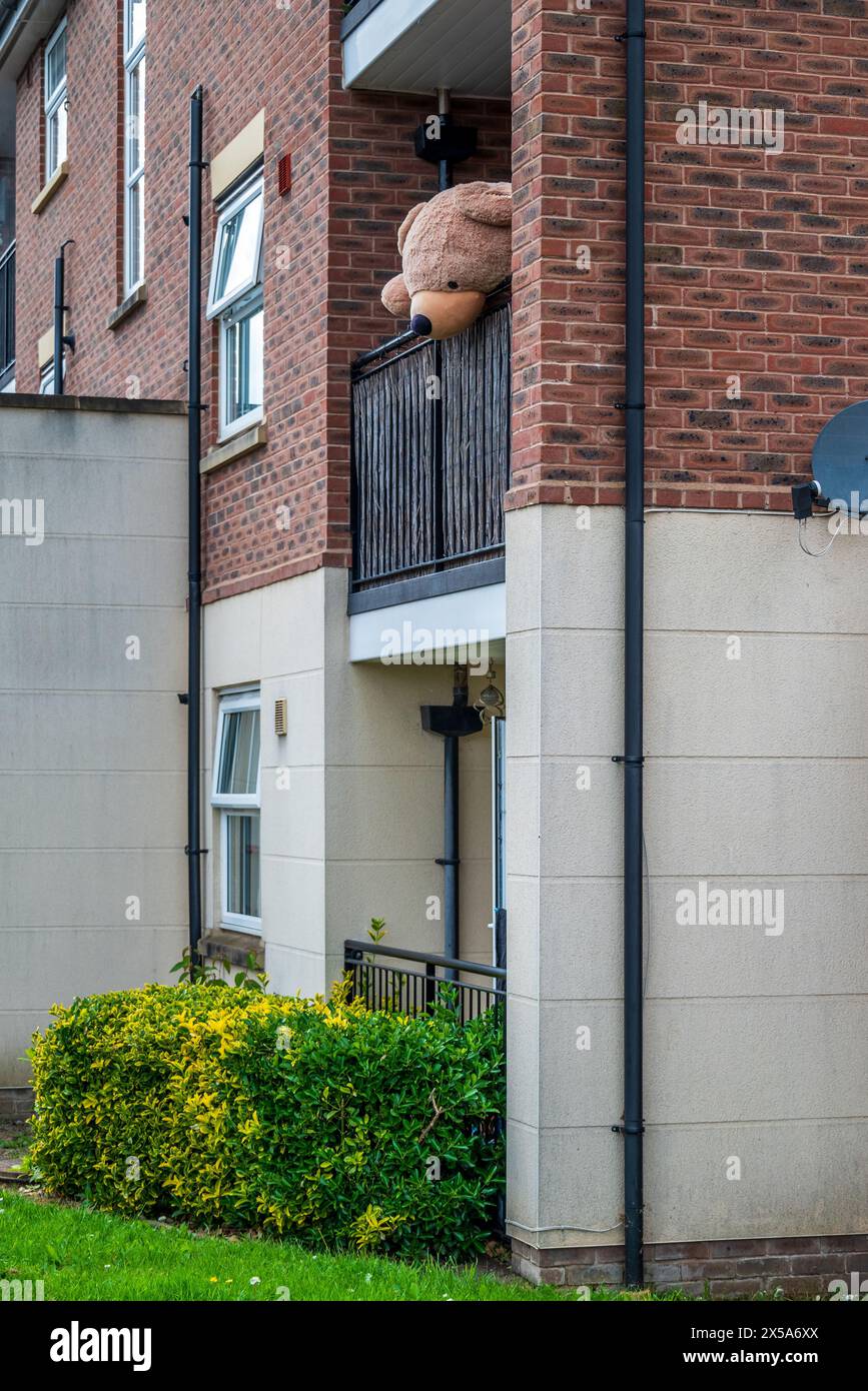 Der riesige Teddybär sucht nach allen Welten, als ob er von diesem Balkon oben fliehen will. Stockfoto