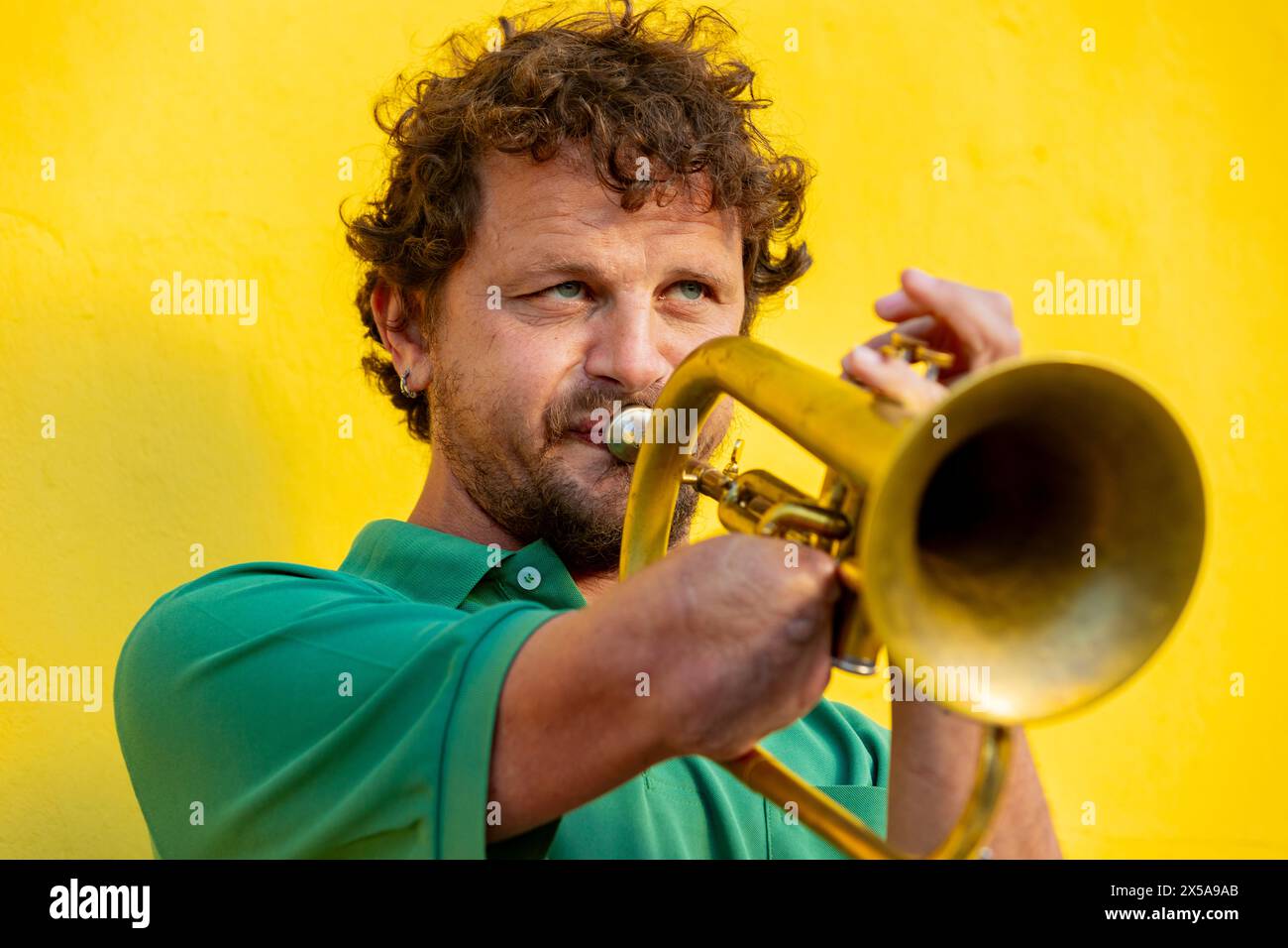 Ein einarmiger Trompeter zeigt sein musikalisches Talent auf einer urbanen Straße und spielt mit Leidenschaft an einer hellgelben Wand. Seine Augen sind offen und fokussiert Stockfoto