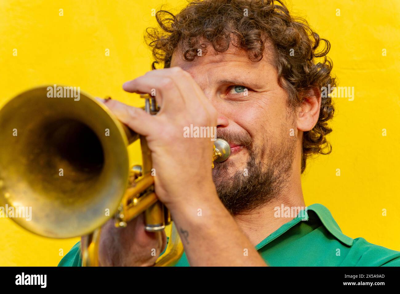 Ein einarmiger Mann mit einem entschlossenen Ausdruck, der vor einem leuchtend gelben Hintergrund Trompete spielt und Widerstandskraft und musikalische Leidenschaft zum Ausdruck bringt. Stockfoto