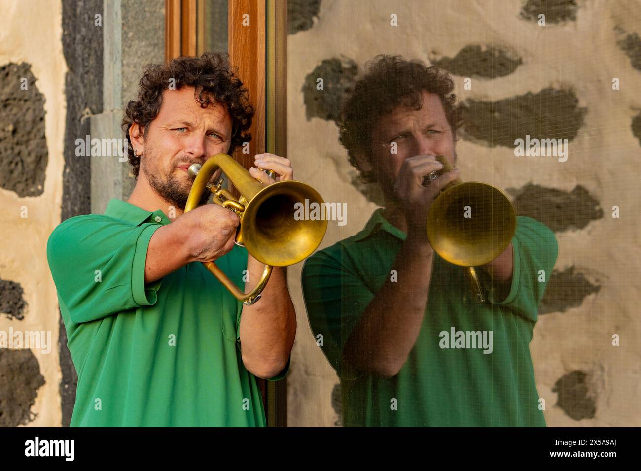 Ein entschlossener, fokussierter einarmiger Trompeter zeigt sein musikalisches Talent auf der Straße, blickt mit offenen Augen von der Kamera weg und reflektiert in einem Windo Stockfoto