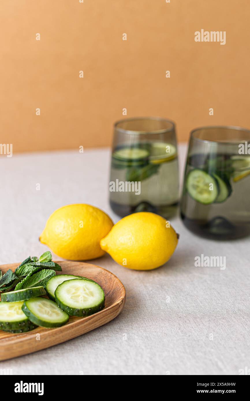 Zwei Gläser gefüllt mit Gurken- und Zitronenwasser, präsentiert mit frischen Zitronen und Gurkenscheiben auf einem Holztablett, was einen gesunden Lifest fördert Stockfoto