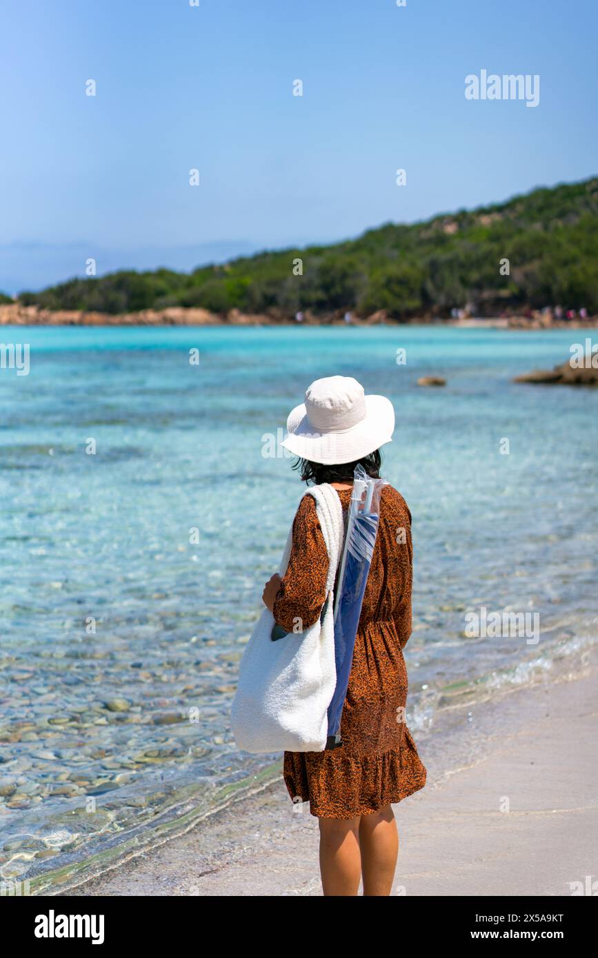 Eine Reisende Frau bewundert das klare Wasser des Strands Grande Pevero mit weißem Sand und der natürlichen Umgebung Sardiniens Stockfoto