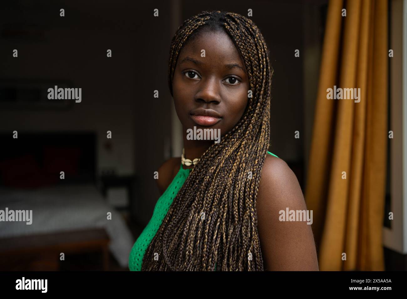 Ein Nahaufnahme-Bild mit einer jungen Afroamerikanerin mit geflochtenen Haaren und einem ruhigen Ausdruck in Innenräumen, das eine entspannte Atmosphäre in der Wohnung darstellt Stockfoto