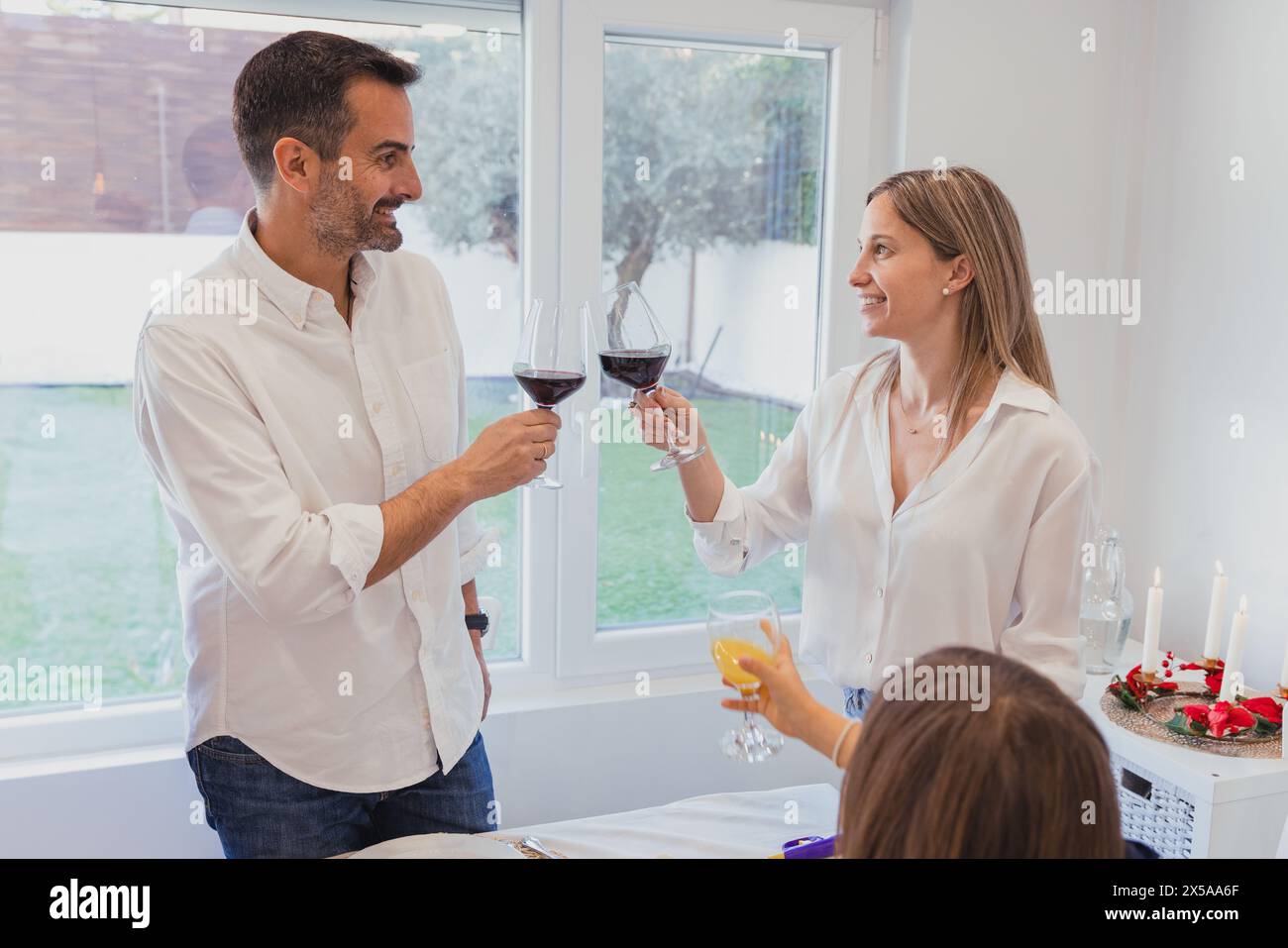 Ein Mann und eine Frau stoßen fröhlich mit Rotweingläsern auf ein festliches Weihnachtsessen der Familie in gemütlicher Atmosphäre an Stockfoto