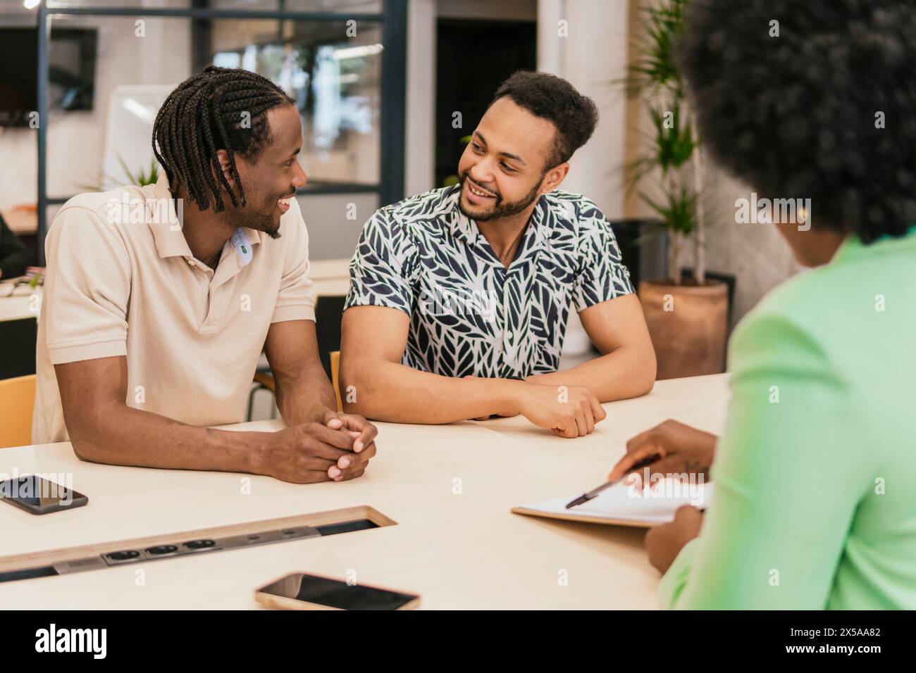 Drei Fachleute führen eine freundliche und kollaborative Diskussion in einer modernen Umgebung des Coworking Space Stockfoto