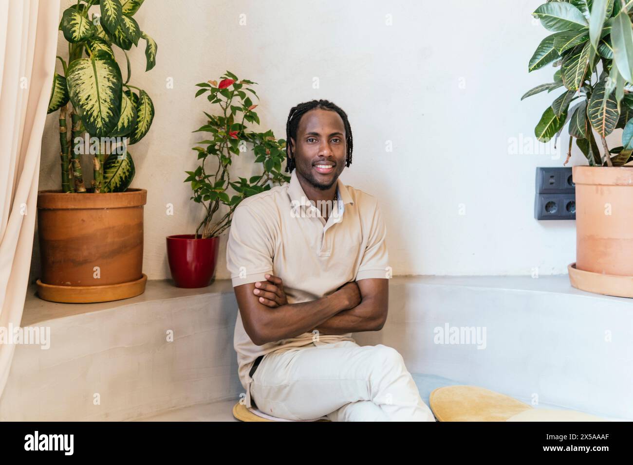 Ein entspannter, professioneller Mann sitzt lässig in einem modernen Coworking-Raum mit dekorativen Pflanzen Stockfoto