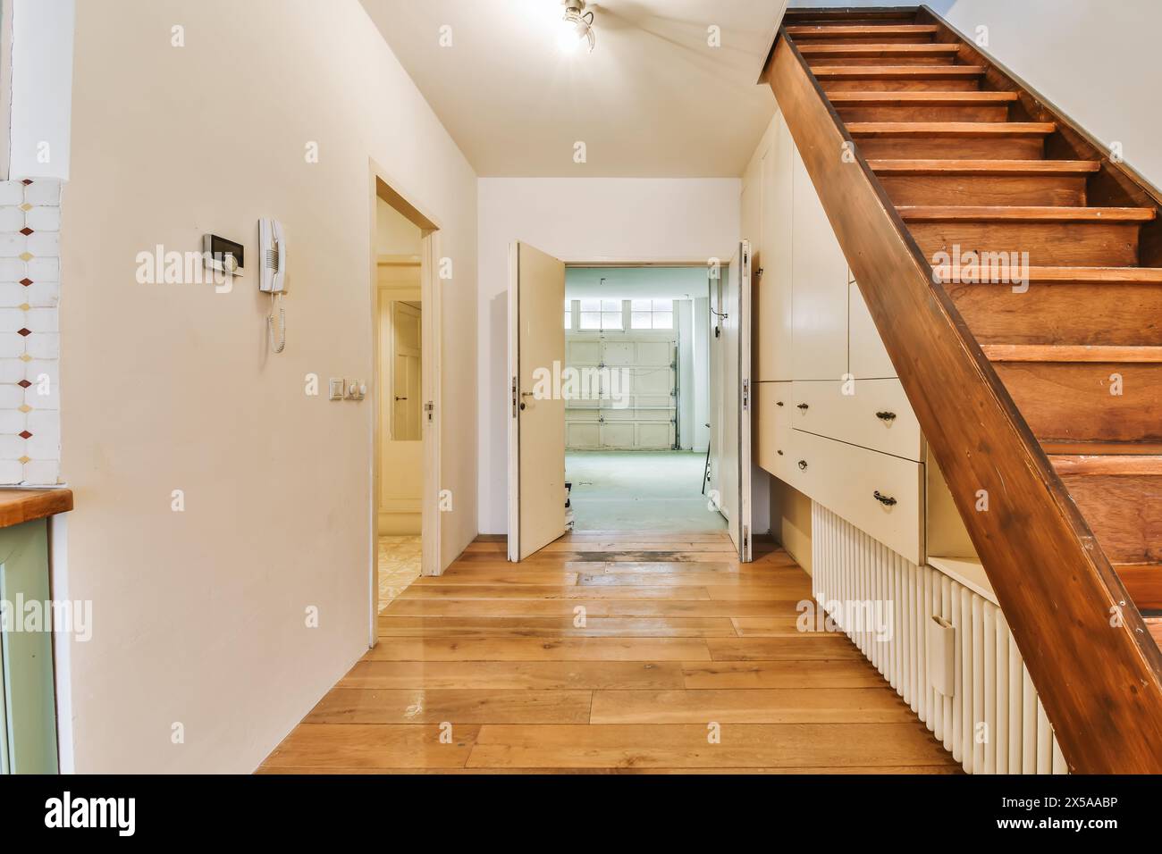 Warme und einladende Inneneinrichtung mit Holztreppe, Hartholzböden und neutralen Wänden, mit offenen Türen, die zu angrenzenden Zimmern führen. Stockfoto