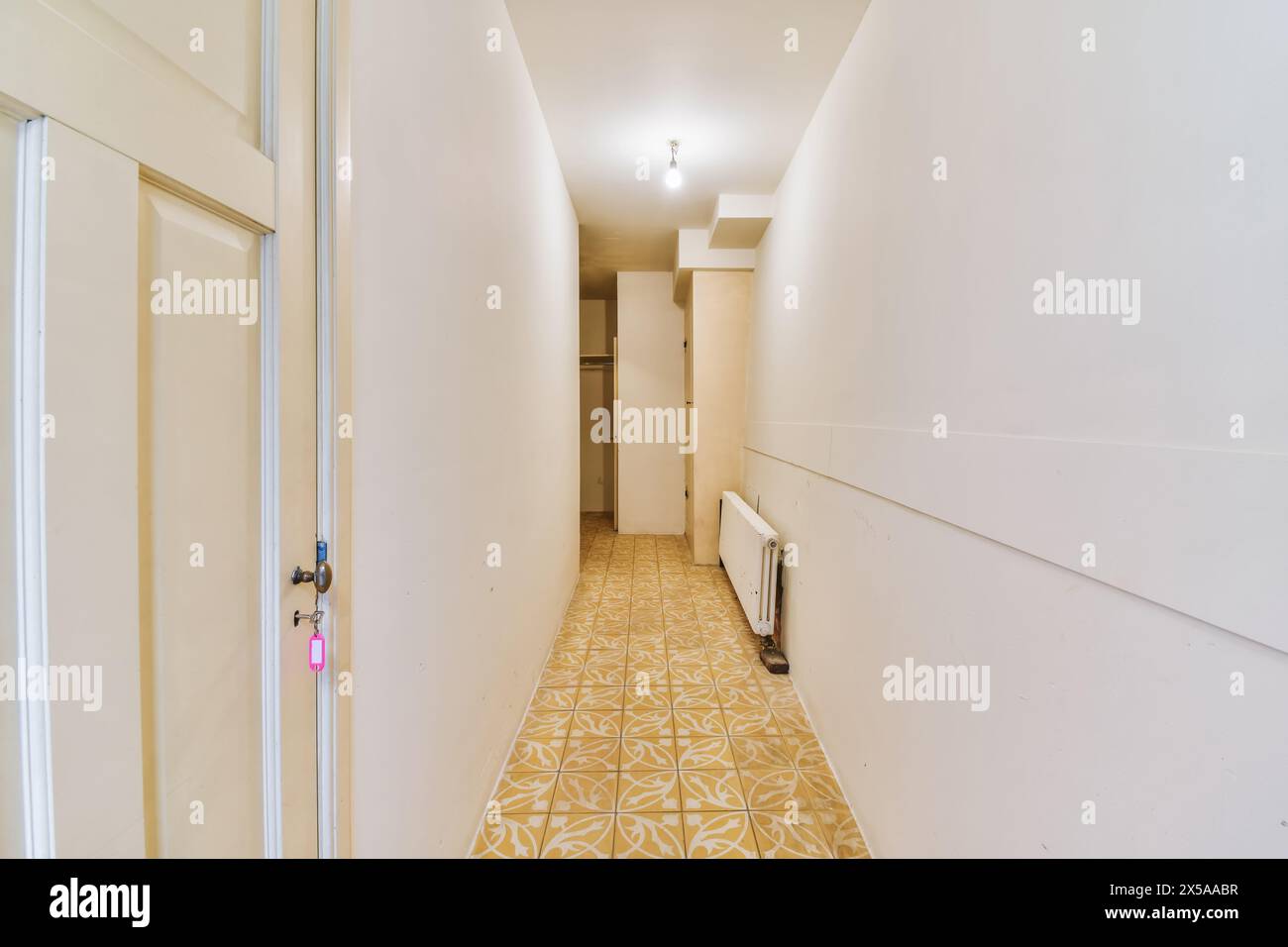 Ein leerer, heller Flur mit weißen Wänden und gelbem Fliesenboden, Türen und Heizkörper. Stockfoto