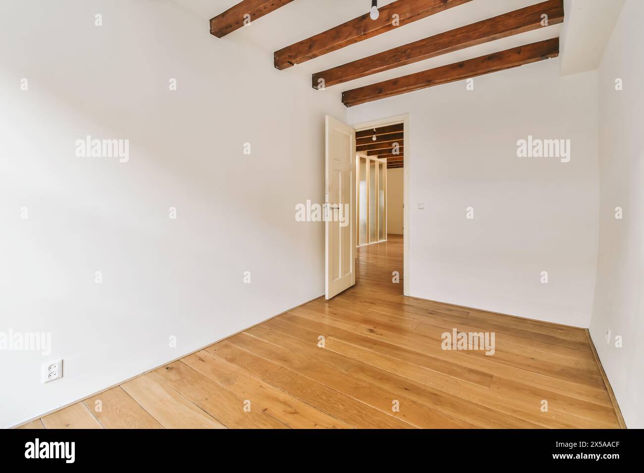 Leeres Zimmer mit poliertem Holzfußboden und sichtbaren Deckenbalken, die ein modernes minimalistisches Interieur schaffen. Stockfoto