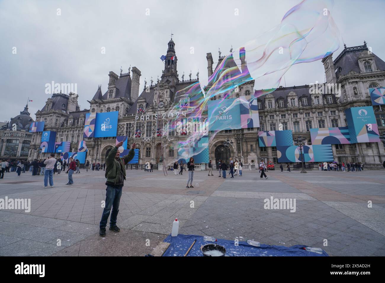 Paris, Frankreich. Mai 2024. Ein Straßenkünstler bläst Seifenblasen vor dem Hotel de Ville, das als Austragungsort der Olympischen Spiele 2024 und der Paralympics in Paris mit einem riesigen Poster geschmückt ist. Quelle: amer Gazzal/Alamy Live News Stockfoto