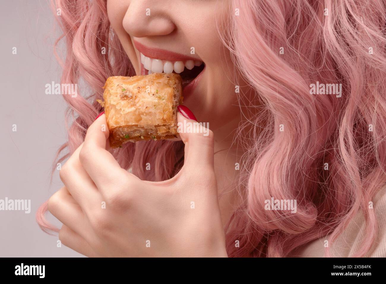 Frau mit rosa lockigen Haaren isst Baklava aus der Nähe. Stockfoto