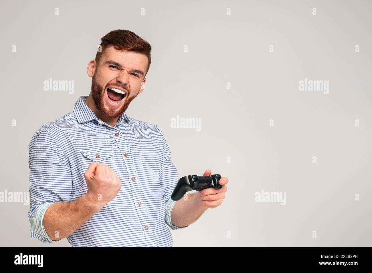 Der junge Mann gewinnt ein Videospiel und fühlt sich glücklich über den Studiohintergrund Stockfoto