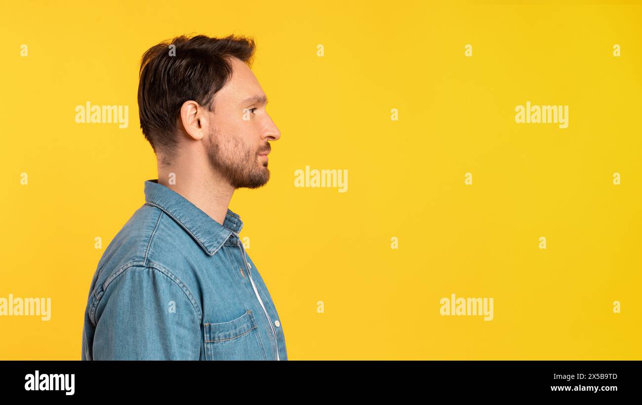 Mann, der vor gelbem Hintergrund steht und den Kopierraum beobachtet Stockfoto