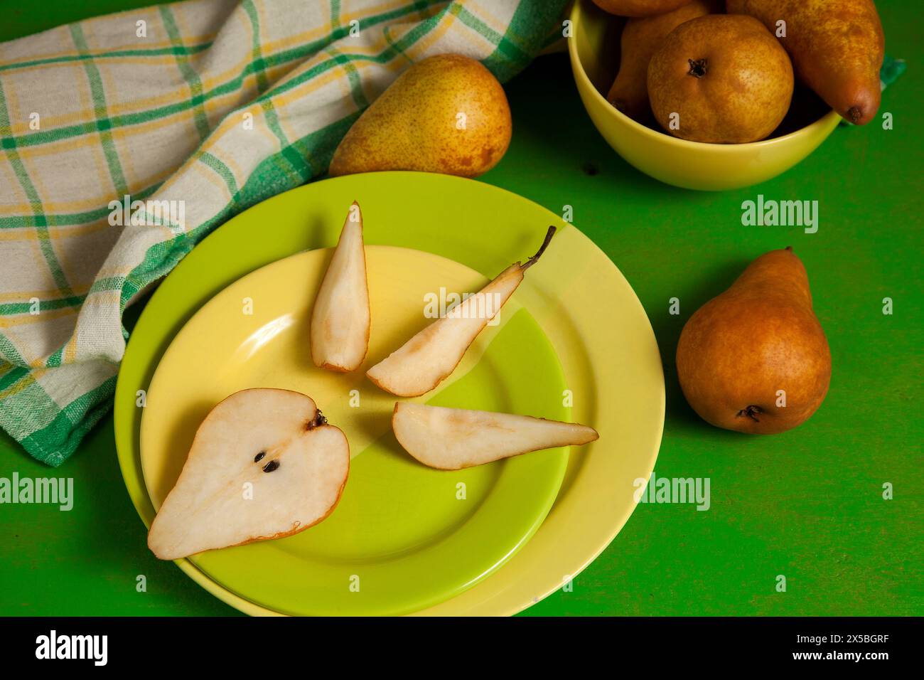 Grüner Teller mit Scheiben und der Hälfte reifer saftiger Birnenfrucht und grünem Küchentuch auf grünem hölzernem Hintergrund. Stockfoto