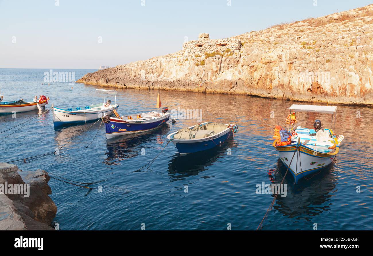 Blue Grotto, Malta - 22. August 2019: Blick auf die Küste des Hafens der Blauen Grotte. Kleine Boote liegen vor alten Befestigungsanlagen an einem sonnigen Morni Stockfoto