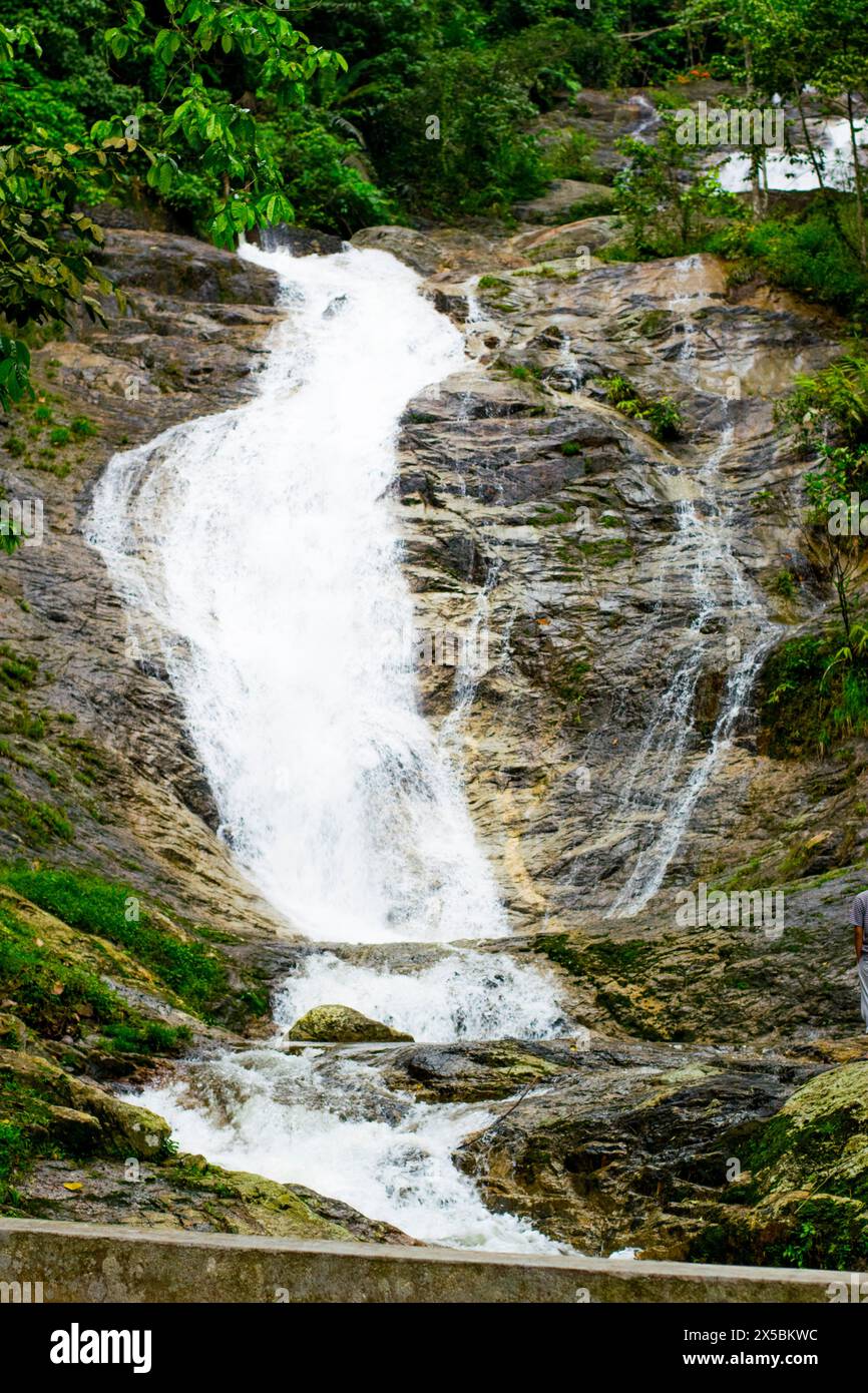 Die ruhige Schönheit eines kleinen Wasserfalls in Malaysia ist ein Touristenziel. Seidenglattes Wasser kaskadiert über Felsen, umgeben von hoch aufragenden Bäumen. Stockfoto