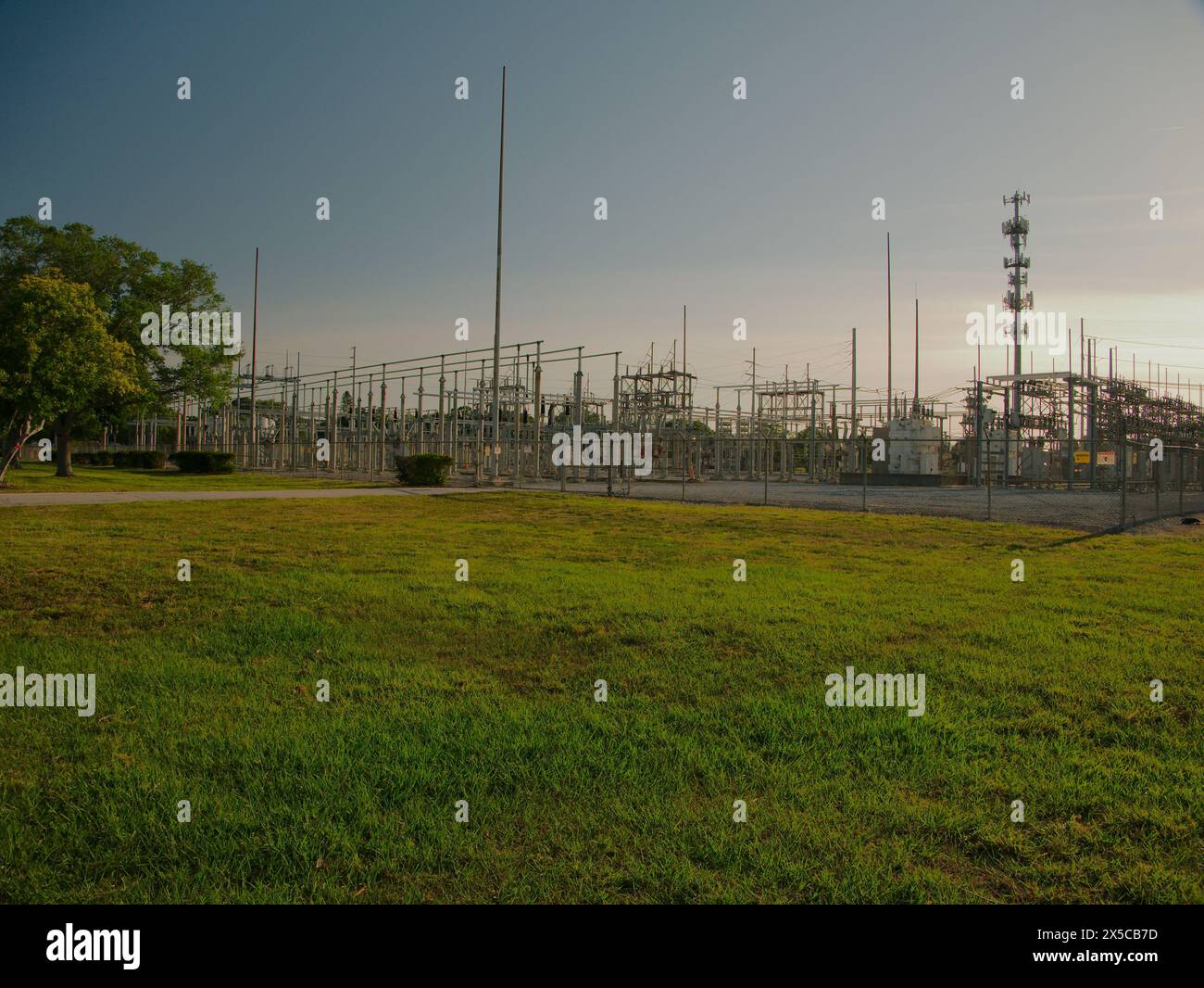 Weite Aussicht bei Sonnenuntergang auf eine elektrische Umspannstation mit Hochspannungsleitungen in St. Petersburg, Florida. Blick auf grünes Gras, blauer Himmel mit großem Metall Stockfoto