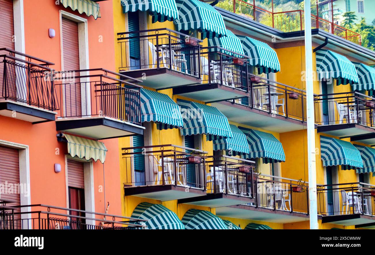 Gardasee, Italien, 16. April 2024: Balkone von Ferienwohnungen mit kleinen gestreiften Markisen und schmiedeeisernen Brüstungen Stockfoto