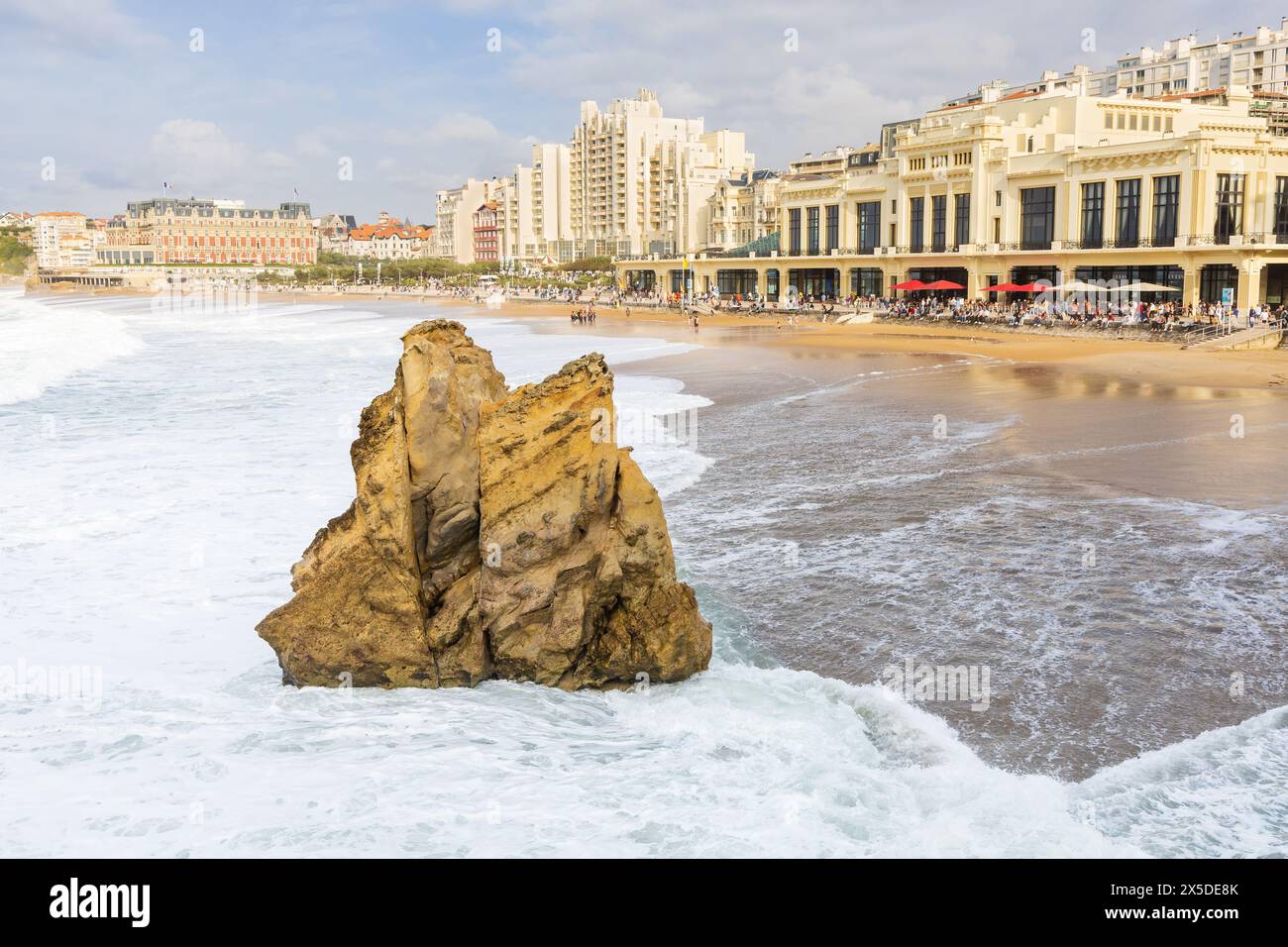 Die schäumenden Wellen stürzen auf den Sandstrand La Grande Plage mit einem gelben Felsen und Gebäude der Stadt im Hintergrund. Biarritz, Frankreich. Stockfoto