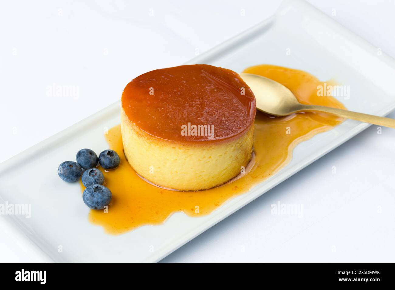 Creme Brulee Dessert serviert mit Sirup und einem Haufen Heidelbeeren auf einem rechteckigen Teller. Stockfoto